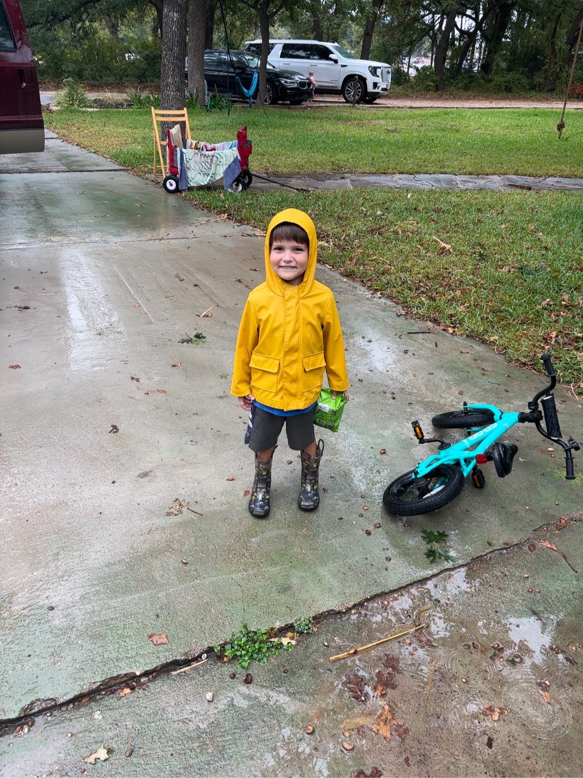 A person in a yellow raincoat stands beside a turquoise bicycle on a wet driveway.